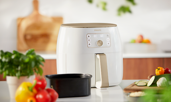 Valkoinen Philips Airfryer XXL ja tuoreita kasviksia ja basilikan lehtiä sen vieressä