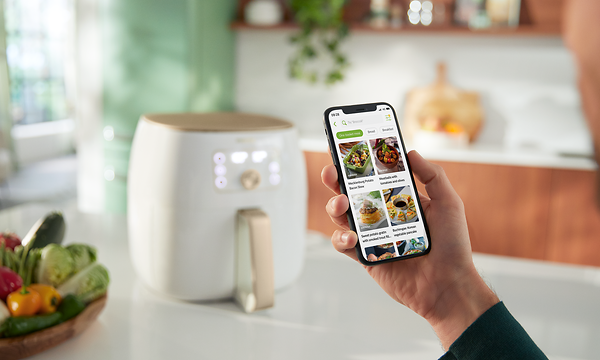 Valkoinen Philips Airfryer XXL -kiertoilmakypsennin pöydällä ja henkilö selaa nutriU-sovellusta