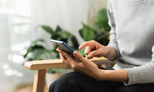 Henkilö käyttää älypuhelintaan VPN-yhteydellä olohuoneessa, jossa on viherkasveja
