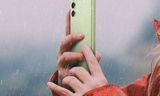 Nainen pitää kädessään vaaleanvihreää Galaxy A54 5G -älypuhelinta sateessa