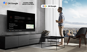 Mies seisoo seinäänkiinnitetyn TCL-television edessä ja käyttää handsfree-ääniohjausta sanomalla 'OK google'