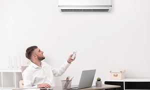 Mies säätää ilmalämpöpumppua kaukosäätimellä toimistossa