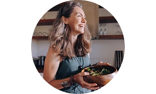 Hymyilevä nainen keittiössä puinen salaattikulho kädessään