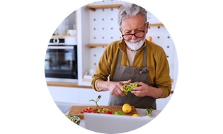 Harmaahiuksinen mies pilkkoo vihanneksia keittiön työtason ääressä