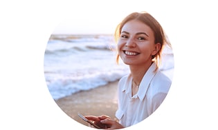 Hymyilevä nainen meren rannalla puhelin kädessään