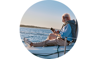Iäkäs mies istuu purjelaivan kannella käytämässä tablet-laitetta