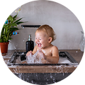 Vauva istuu vedellä täytetyssä tiskialtaassa ja loiskuttaa vettä iloisesti