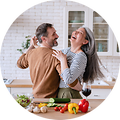 Nainen ja mies tanssivat yhdessä keittiössään samalla nauraen