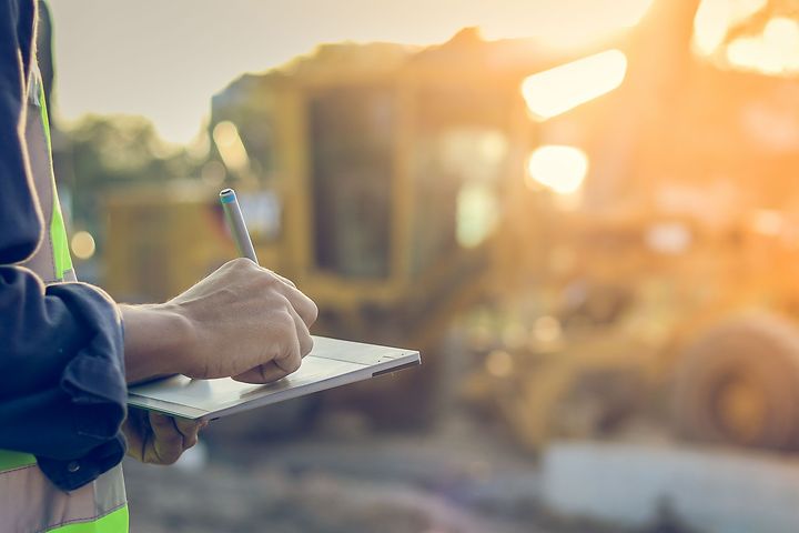 Työvaatteisiin pukeutunut rakennusalan työntekijä tekee muistiinpanoja tabletille