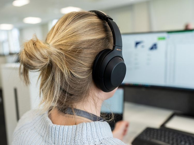 Kuulokkeet päässä oleva nainen istuu tietokone näytön edessä