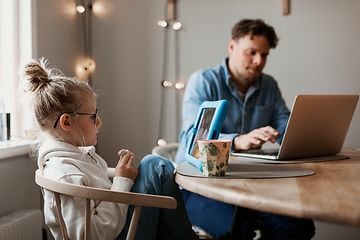Isä ja tytär käyttävät tietokoneitaan keittiön pöydän ääressä