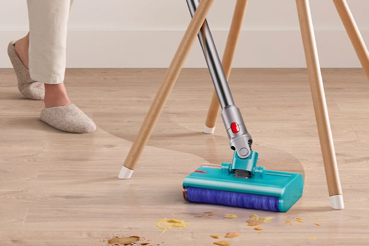 Nainen puhdistaa keittiön laminaattilattiaa Dyson V15 Submarine -imurilla