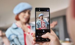 Sony Xperia 5 V -älypuhelin ja kuvaajalle poseeraava nainen