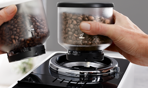 Lähikuva kädestä, joka asettaa Delonghi Rivelia -kahvikoneen papusäiliötä paikalleen