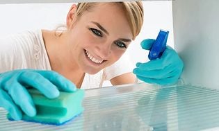 Hymyilevä nainen puhdistamassa jääkaappia suihkeella ja sienellä