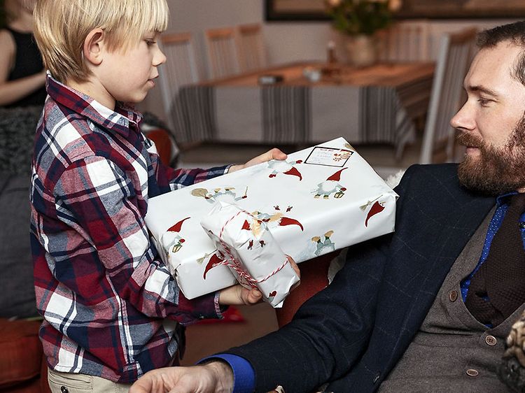 Pieni poika ojentaa joululahjan sohvalla istuvalla isälleen