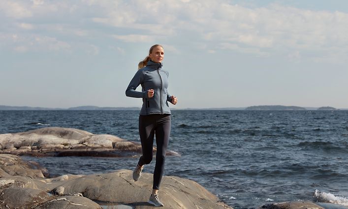 Nainen juoksee kallioisella merenrannalla urheiluvaatteissa