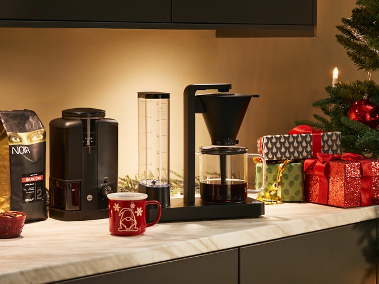 Kahvinkeitin ja kahvimylly joulukoristeiden ja lahjojen vieressä keittiön pöydällä