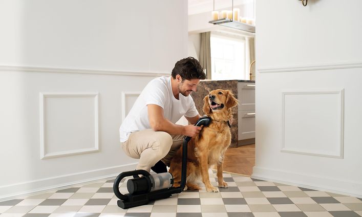 Mies imuroi koiransa turkkia Nilfisk S1 Pet Care -imurilla, johon on liitetty harjasuutin joustavalla letkulla