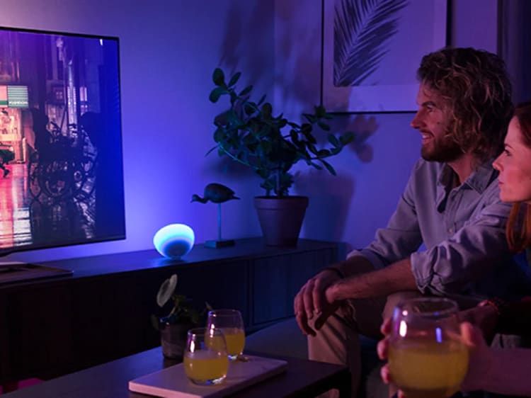 Neljä ihmistä katsoo televisiota sinivioletin Philips Hue -tunnelmavalaistuksen ympäröimänä