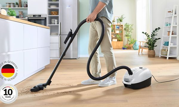 Mies imuroi keittiön lattiaa Bosch Series 4 -pölynimurilla, kuvan vasemmassa alareunassa logo 10 vuoden moottoritakuulle