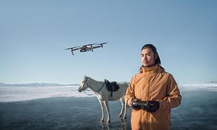 Mies lennättää dronea tunturissa. Valkoinen hevonen taustalla.