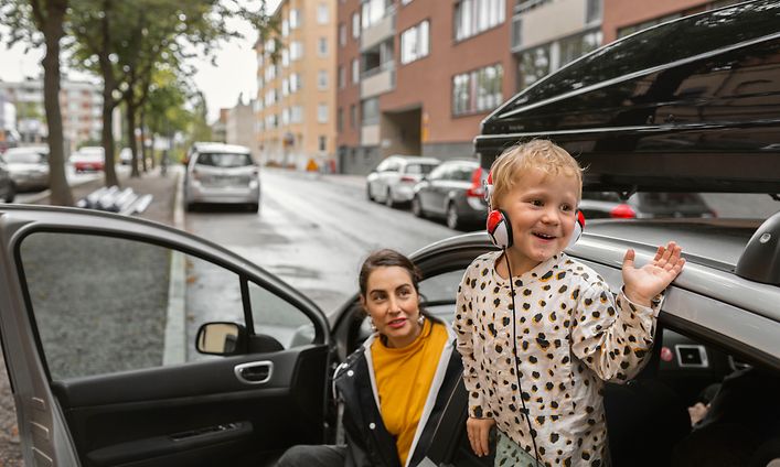 Kuulokkeet päässä oleva lapsi vilkuttaa auton ikkunasta