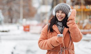 Kuulokkeet päässä oleva tyttö matkapuhelin kädessään nauttimassa ulkoilmasta talvipäivänä