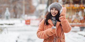 Kuulokkeet päässä oleva tyttö matkapuhelin kädessään nauttimassa ulkoilmasta talvipäivänä