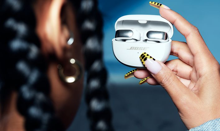 Avoimet Bose Ultra -nappikuulokeet - naisella on käsissään open-ear-nappikuulokkeet