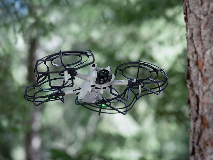 Tietokoneet - DJI - DJI Mini 4 Pro -drone suojuksilla lentämässä metsässä