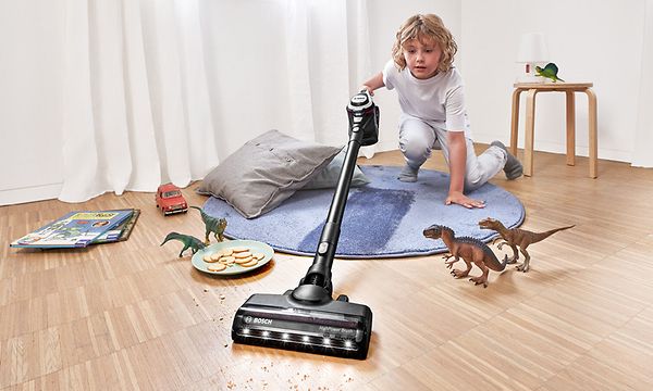 Pieni poika puhdistaa lattiaa lelujensa ympäriltä Bosch-varsi-imurilla