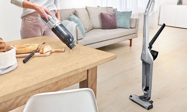 Nainen käyttää Bosch Serie 4 Flexxo -varsi-imurin rikkaimuriosaa murujen puhdistamiseen ruokapöydältä