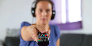 Kuulokkeet päässään oleva nainen osoittaa kaukosäätimellä televisiota