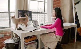 Nainen työskentelee kannettavalla tietokoneella pöydän ääressä istuen