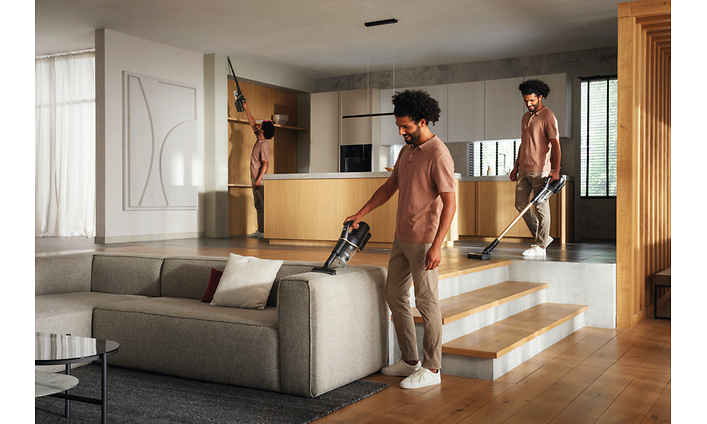 Miele Duoflex HX1 -johdoton varsipölynimuri ja mies imuroimassa olohuoneen sohvaa
