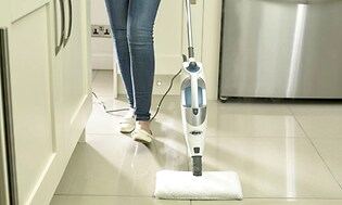 Nainen käyttää höyrypuhdistinta keittiön lattian puhdistamiseen