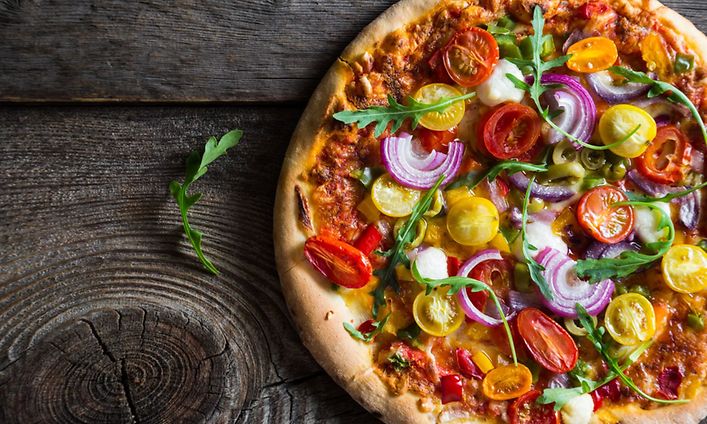 Kasvispizza, jossa punasipulia, tomaattia ja ruccolasalaattia asetettu puiselle pöydälle