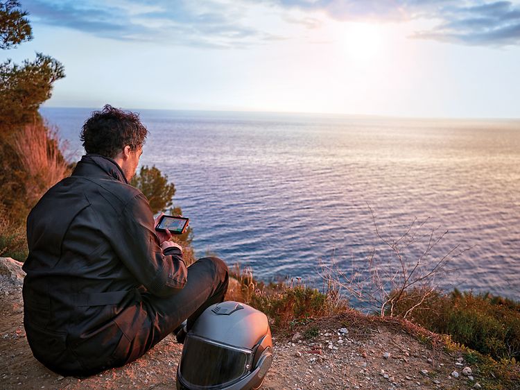 Mies istuu meren rannalla Garmin Zumo XT -navigaattori kädessään