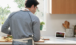 Mies laittaa ruokaa Google Nest Hub -näyttöä katsellessaan