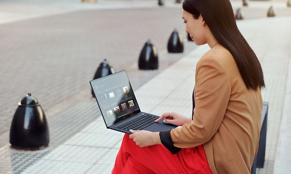 Nainen istuu ulkona kivisen kadun vieressä olevalla puistonpenkillä ja työskentelee HP EliteBook -kannettavalla