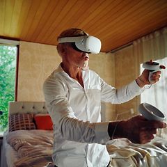 Valkoiseen kauluspaitaan pukeutunut mies pelaa VR-lasit päässään