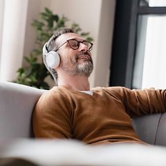 Mies istuu silmat suljettuina sohvalla ja nauttii musiikista kuulokkeet korvillaan