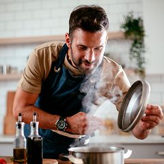 Mies nostaa kattilan kantta tarkastaakseen ruokaa joka valmistuu keittotasolla