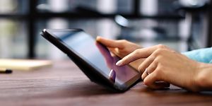 Nainen työskentelee tabletilla, jota hän pitelee kädessään