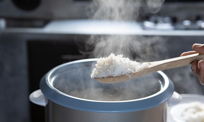 Avoin riisikeitin, josta henkilö nostaa valmista riisiä puulusikalla