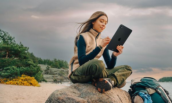 Nainen istuu rannalla olevan kiven päällä iPadin kanssa
