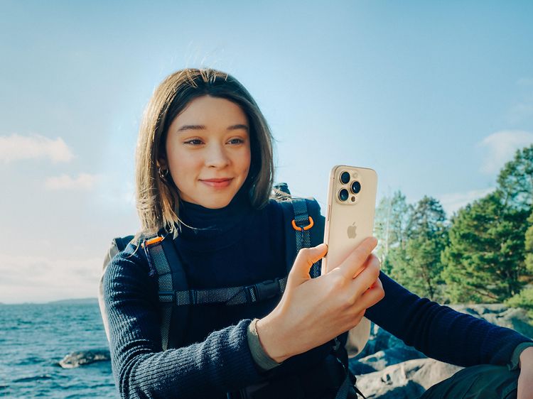 Reppu selässä oleva nainen repussa pitelee iPhone 16 Pro -älypuhelinta