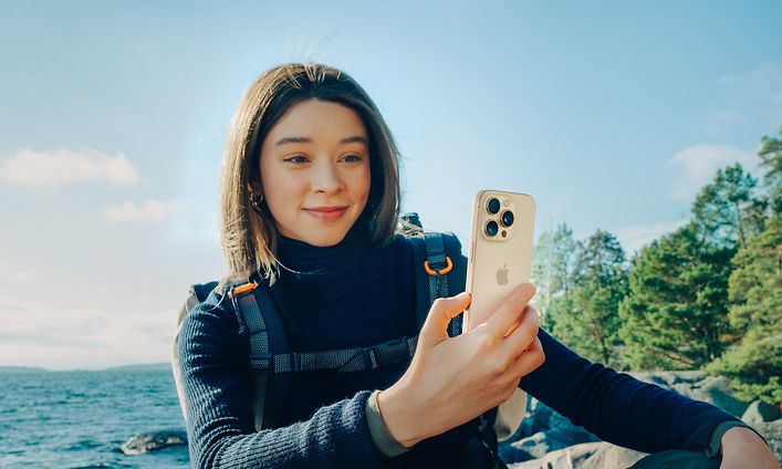 Reppu selässä oleva nainen repussa pitelee iPhone 16 Pro -älypuhelinta