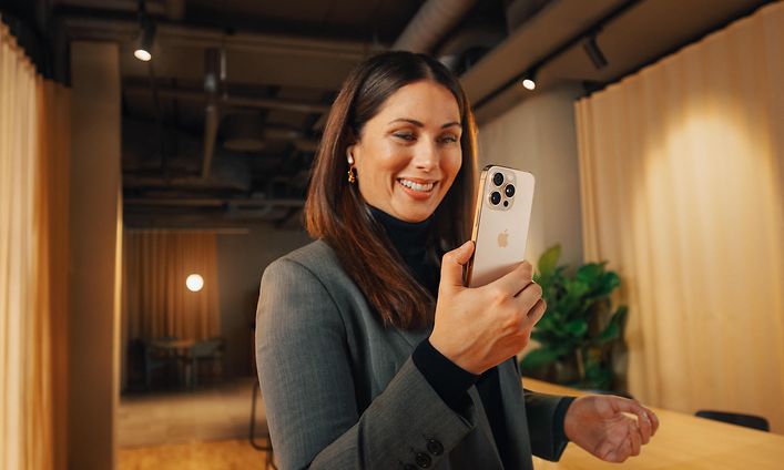 Hymyilevä liikenainen käyttää iPhone 16 Pro -puhelintaan
